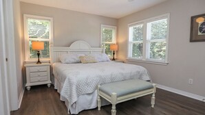 Une chambre à coucher avec un lit, des tables de chevet, un banc et des fenêtres équipées de stores.