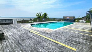 A wooden deck with a swimming pool, a lifeguard stand, and a view of the ocean.