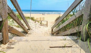 A wooden beach entrance leading to a sandy beach with a bench and a table in the middle.