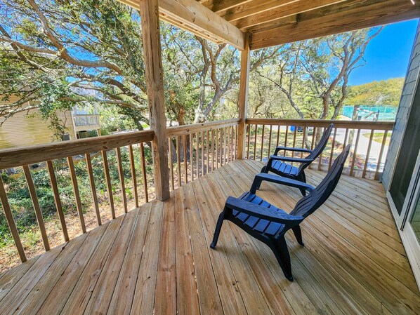 A wooden deck with two black lounge chairs, surrounded by a wooden railing and trees.