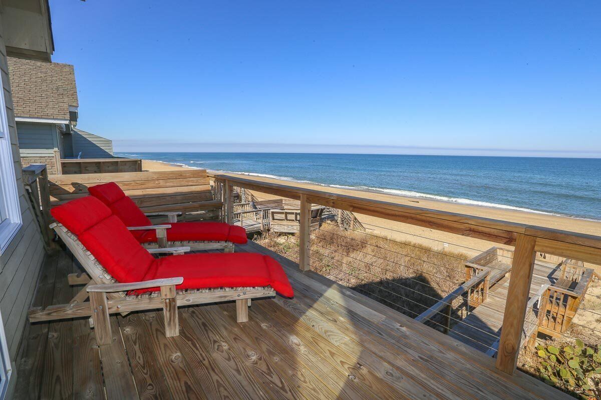 A wooden deck with two red lounge chairs facing the ocean.