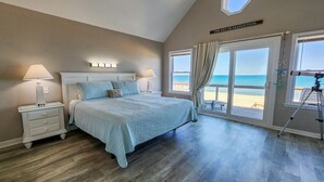 A bedroom with a large bed, a nightstand, a ceiling fan, and a view of the beach through large windows. - 🏖️ Someplace Else - Oceanfront 4 BR Townhome w/Gorgeous Sunrise Views 🌅 (Southern Shores)