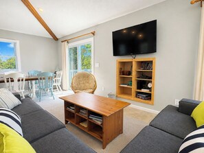 Ett vardagsrum med en soffgrupp, ett soffbord i trÀ, en tv som Àr monterad pÄ vÀggen och en bokhylla.