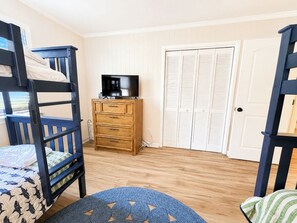 A room with bunk beds, a television, a wooden dresser, and a closet with louvered doors. - Capt'n Rons - 🏖️ 4BR Southern Shores Oceanside home w/Private Pool 🏖️ (Southern Shores)