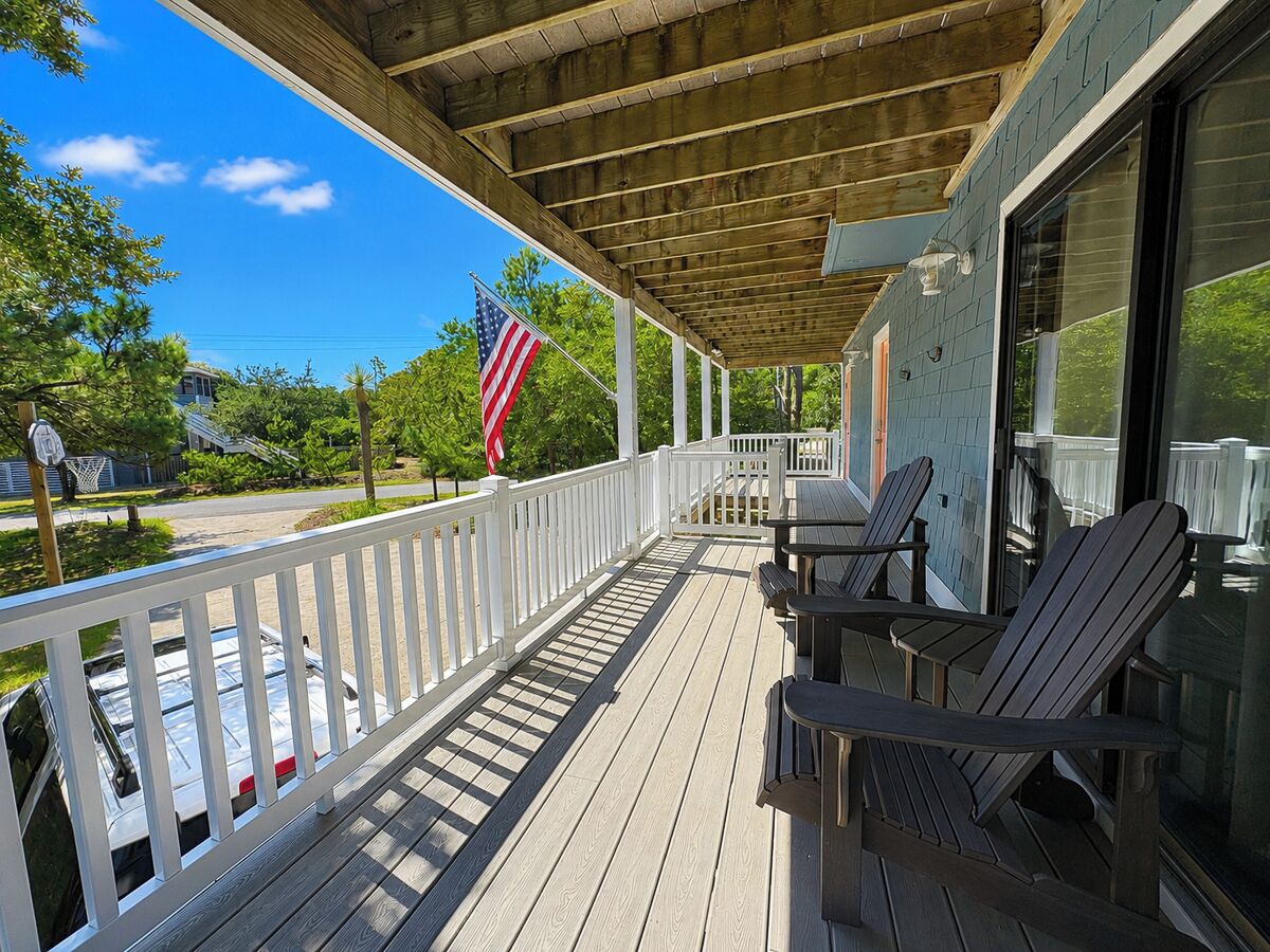 A covered porch with a railing, outdoor seating, and a view of a residential street.