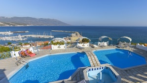 A pool area with two separate pools, lounge chairs, and a view of the sea. - Pavlis Studios Ormos (Samos)