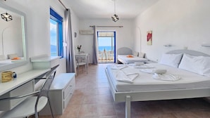 A hotel room with a bed, a desk, a chair, a small table with a vase, and a view of the sea. - Pavlis Studios Ormos (Samos)