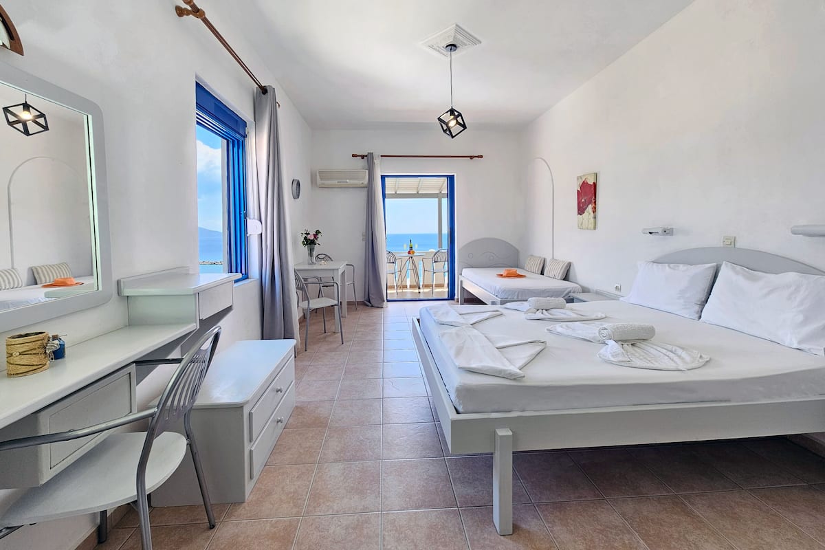 Une chambre d’hôtel avec un lit, un bureau, une chaise, une petite table avec un vase et une vue sur la mer.