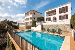 A poolside view of a hotel with a swimming pool, outdoor seating, and a two-story building with balconies.