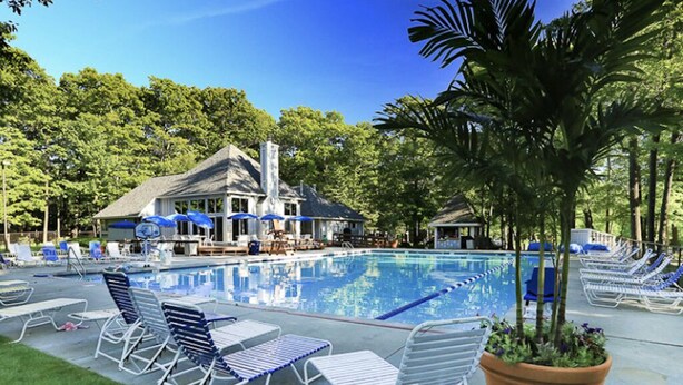 A swimming pool with lounge chairs and umbrellas, surrounded by trees and a building with a chimney. - Summer Getaway: Hiking, Swimming, Fishing, Biking, Golfing, Ski In/Out + more (Hidden Valley)