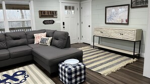 A modern living room with a sectional sofa, a small ottoman, a decorative console table, and a rug. - Lake Daze, Blue Cottage <1mile to Jamestown Marina with space to trailer boat. (Jamestown)