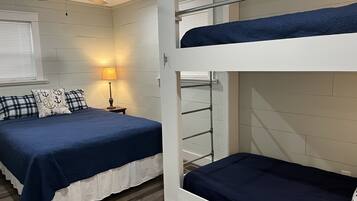 A bunk bed room with a ceiling fan, a bedside lamp, and a window with blinds.