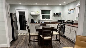 A modern kitchen with white cabinets, a dining table with chairs, a refrigerator, microwave, stove, and a sink. - Lake Daze, Blue Cottage <1mile to Jamestown Marina with space to trailer boat. (Jamestown)