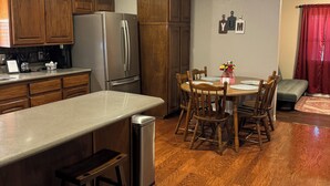 A kitchen with wooden cabinets, a refrigerator, and a coffee maker. There is a dining table with chairs and a vase with flowers.