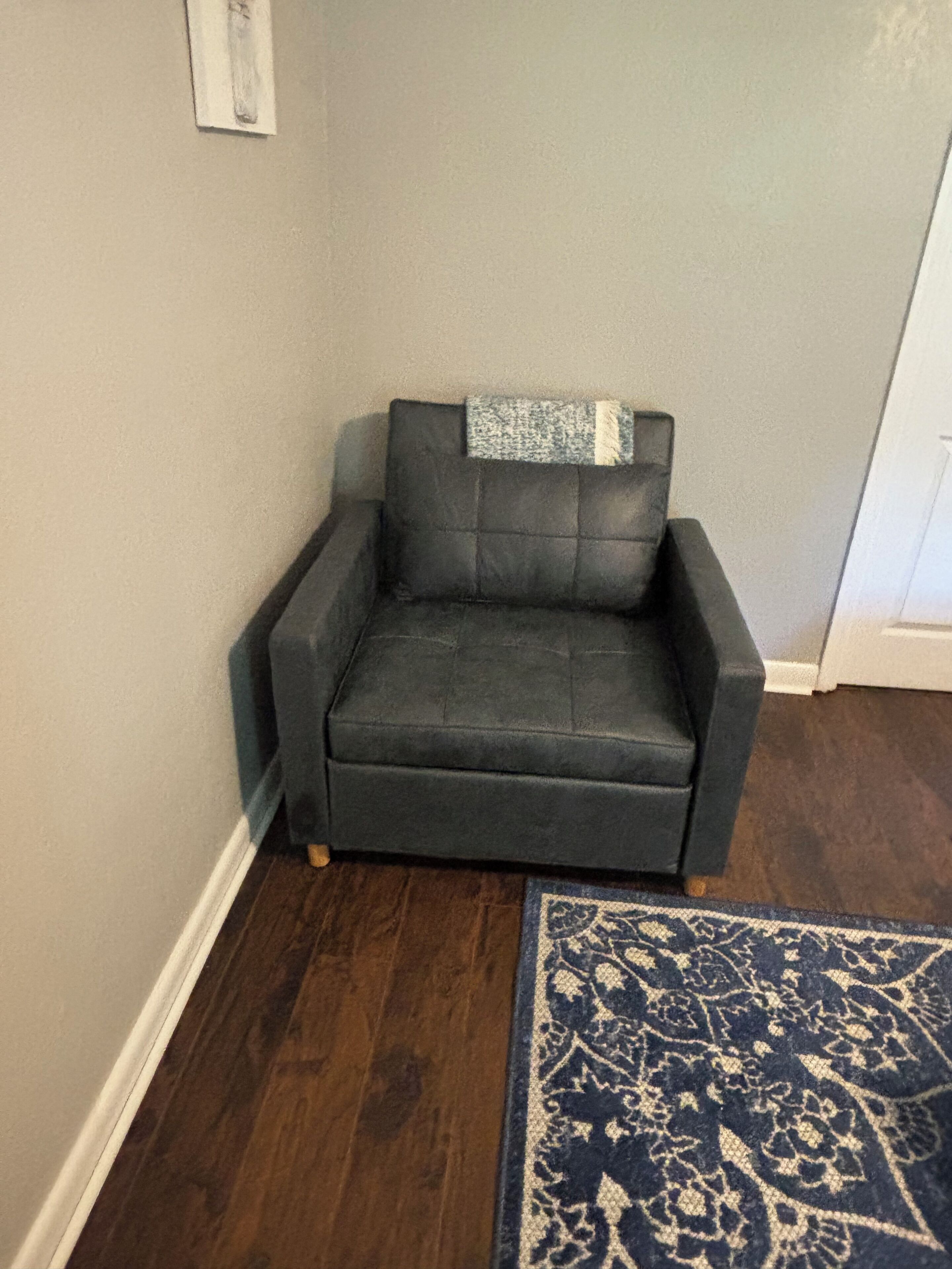 A corner room with a dark grey sofa, a patterned rug, and a white door.