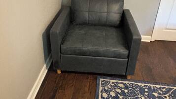 A corner room with a dark grey sofa, a patterned rug, and a white door.