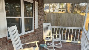 A covered porch with white rocking chairs and a small table.