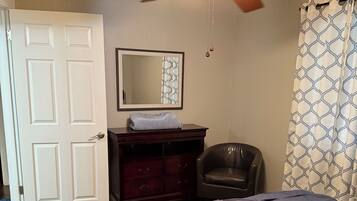A bedroom with a bed, a dresser, a chair, a ceiling fan, and a mirror.