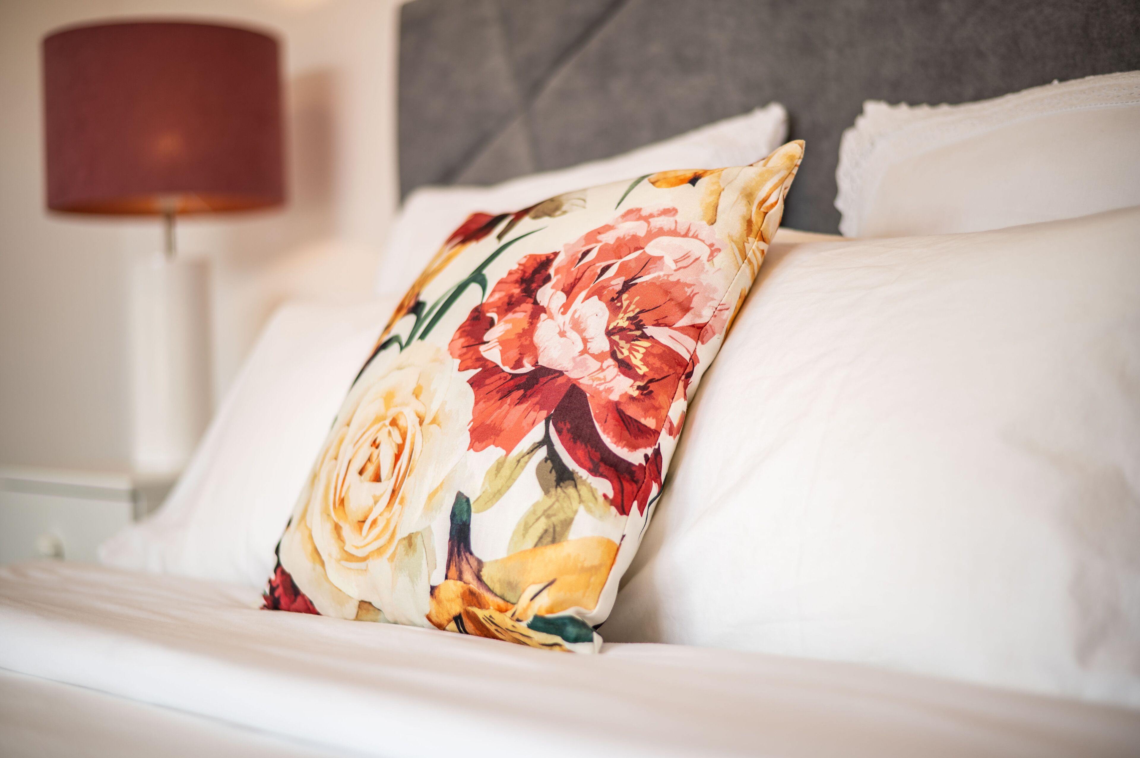 Un lit bien fait, agrémenté d’un coussin à motifs floraux et d’un coussin blanc.