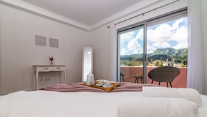 Camera d'albergo con un letto, un comodino con vassoi per la colazione, una sedia e un'ampia finestra vista montagna.