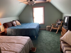 Un dormitorio ático acogedor con una cama grande, una cama más pequeña, un televisor y una silla de madera.