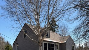 A two-story house with a large tree in front, a front porch, and a visible garage.