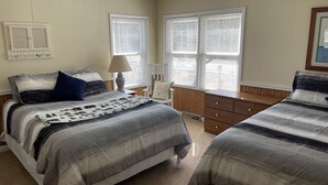 A bedroom with two beds, a dresser, a chair, and a window with blinds.