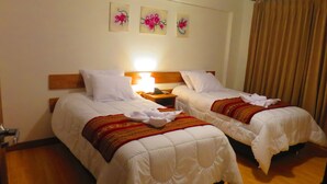 Habitación de hotel con dos camas, una mesita de noche, una lámpara y tres cuadros de flores colgados en la pared.