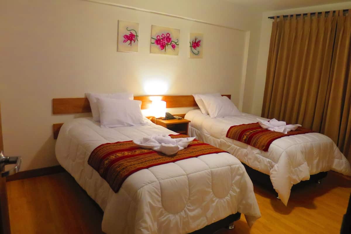 Une chambre d’hôtel avec deux lits, une table de chevet, une lampe et trois tableaux représentant des fleurs, accrochés au mur.