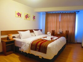 Une chambre d’hôtel avec un grand lit, une table de chevet avec une lampe, une tête de lit en bois et trois tableaux aux motifs floraux accrochés au mur.