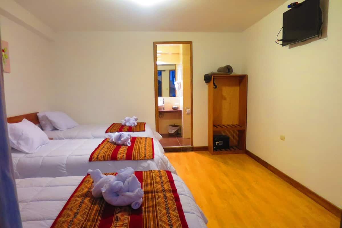 Une chambre d’hôtel avec deux lits, chacun recouvert de draps blancs et de couvertures à motifs rouges et dorés. On y trouve un meuble en bois et un téléviseur fixé au mur.