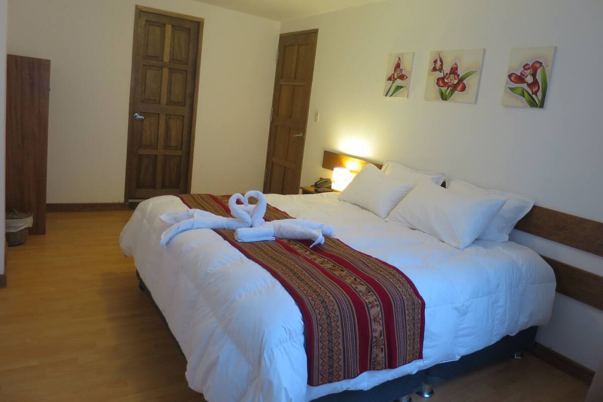 Une chambre d’hôtel avec un grand lit, des portes en bois, une lampe de chevet et trois tableaux représentant des motifs floraux accrochés au mur.