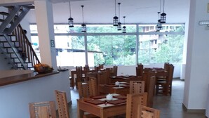 Un amplio comedor con mesas y sillas de madera, ventanas grandes que ofrecen vista a zonas verdes, y una escalera a la izquierda.