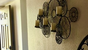 A hallway with a decorative wall piece featuring circular patterns and candle holders, a door with a modern handle, and a metal bed frame.