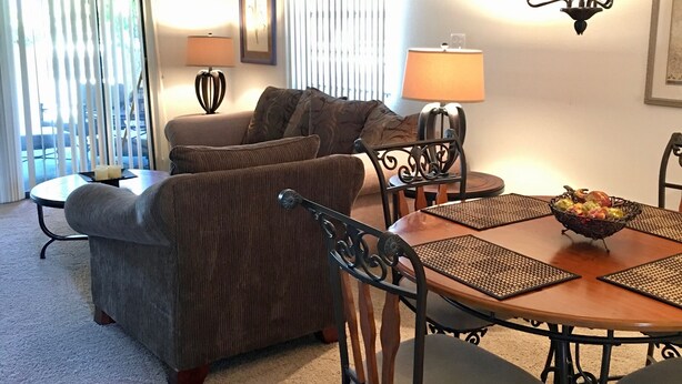 A living room with a sofa, a dining table with chairs, a chandelier, and a ceiling fan.