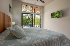 A bedroom with a large bed, a TV on the wall, and a view of the outdoors. - Secluded Luxury Rainforest Villa on the Baru River close to Dominical Beach ! (Dominical)