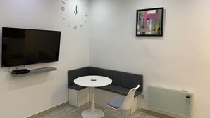 A modern room with a flat-screen TV, a round table, a grey sofa, and a wall clock. - Charming apartment in the old center of Madrid (Madrid)