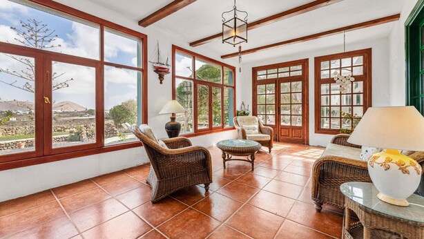 Una habitación amplia con ventanas grandes, muebles de mimbre y suelo de baldosas.