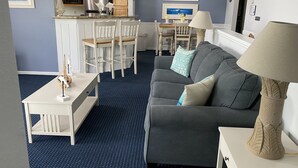 Un espacio habitable compacto con kitchenette, comedor y zona de estar con sofá y lámpara.