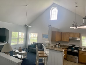 A spacious living area with a high ceiling, a dining table, a sofa, and a kitchen with wooden cabinets and a stove.