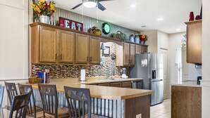 Een moderne keuken met houten kasten, een centraal eiland met barkrukken, een koelkast en een klok aan de muur.