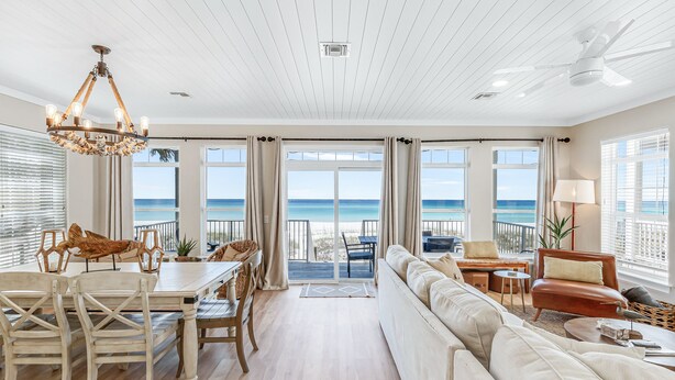 A spacious living room with a large sofa, dining table, and chairs, a chandelier, and a view of the ocean.