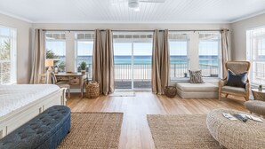 A spacious bedroom with a large bed, a desk, a chair, and a view of the ocean through large windows.
