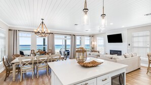 A spacious living area with a large island, dining table, and chairs, a sofa, a TV, and a view of the ocean.