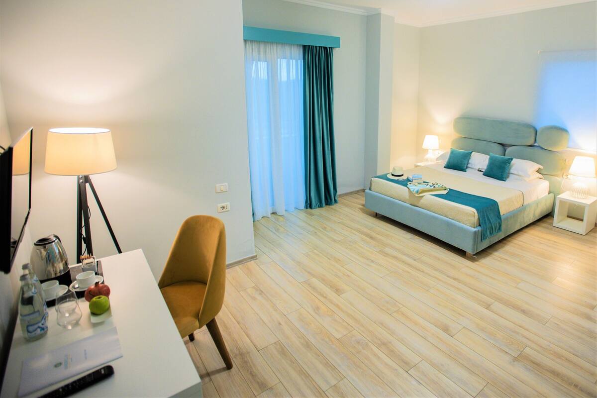 A hotel room with a bed, a desk, a chair, and a lamp.