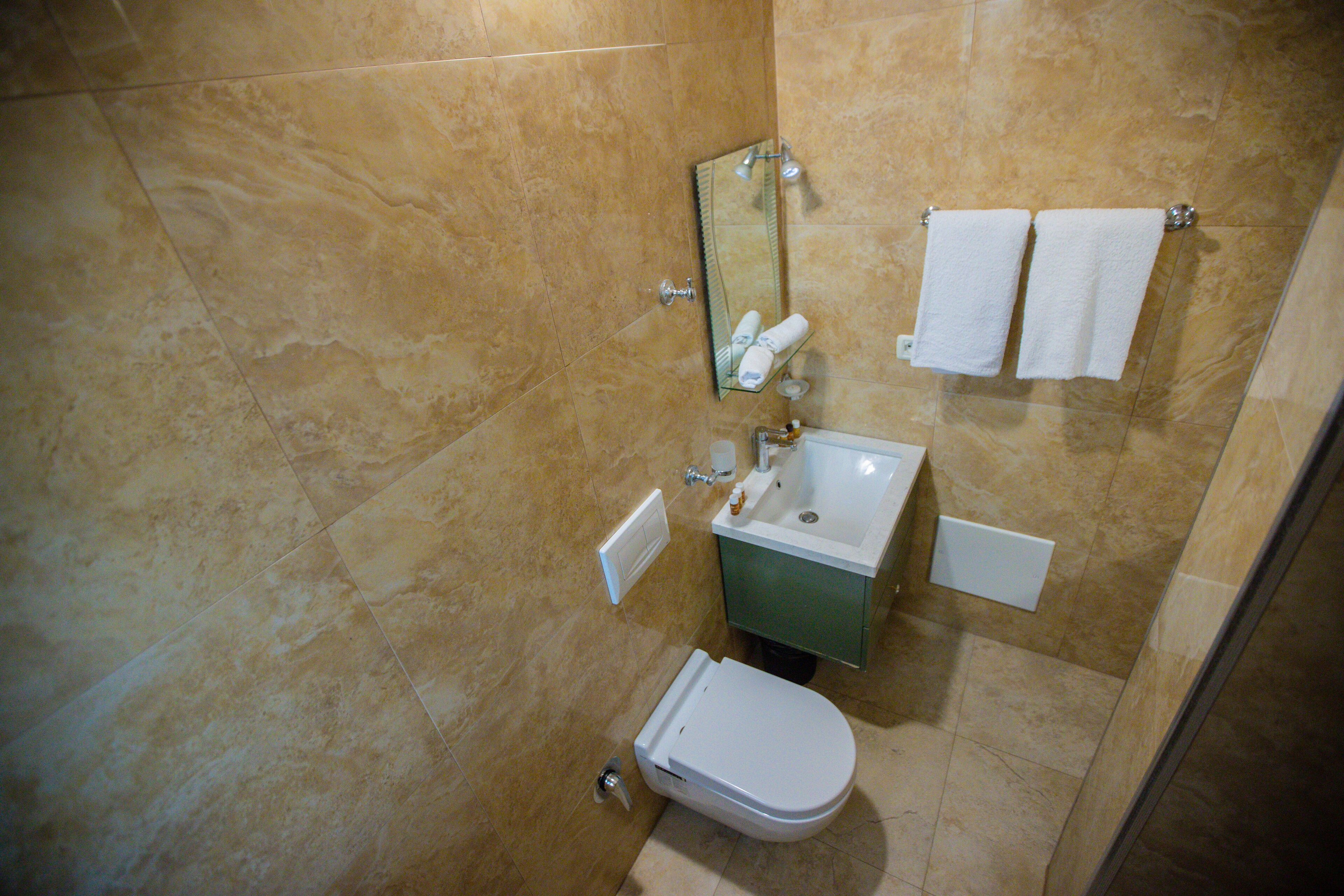 Ein Badezimmer mit Toilette, Waschbecken und Spiegel. Zwei Handtücher hängen an der Wand.