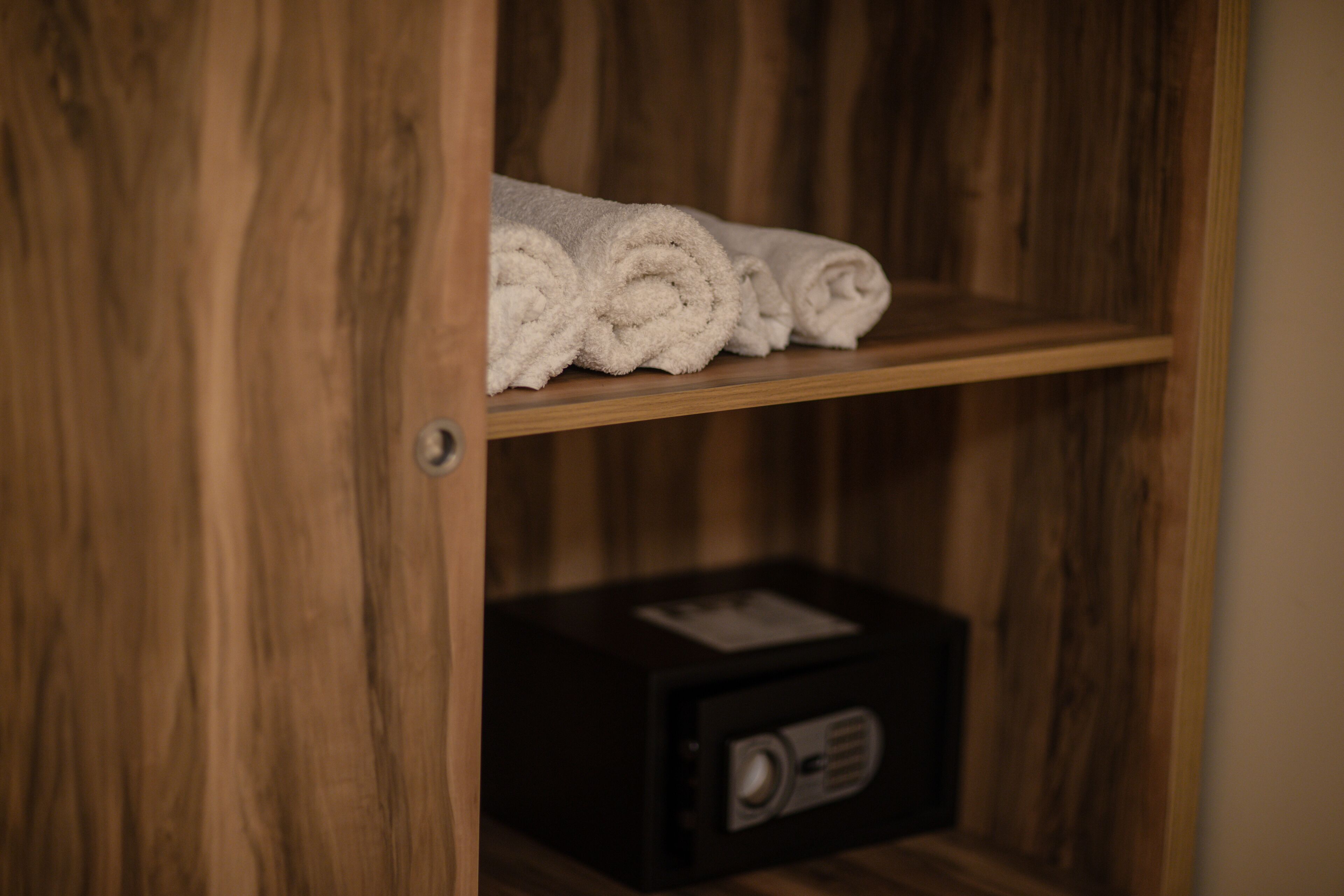 A wooden shelf with rolled towels and a black radio in a wooden cabinet.