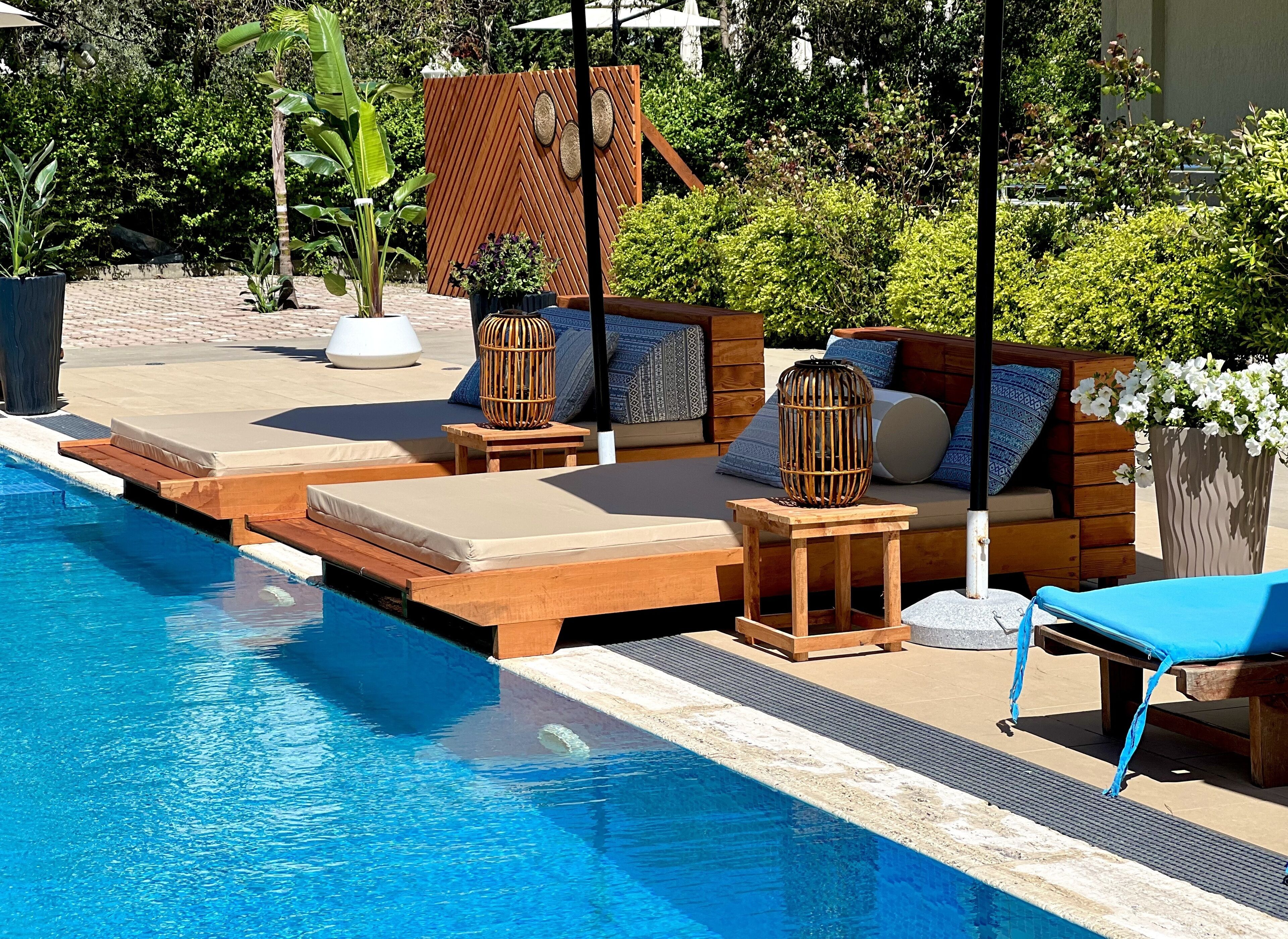 A poolside area with wooden loungers, a small table, and a potted plant.
