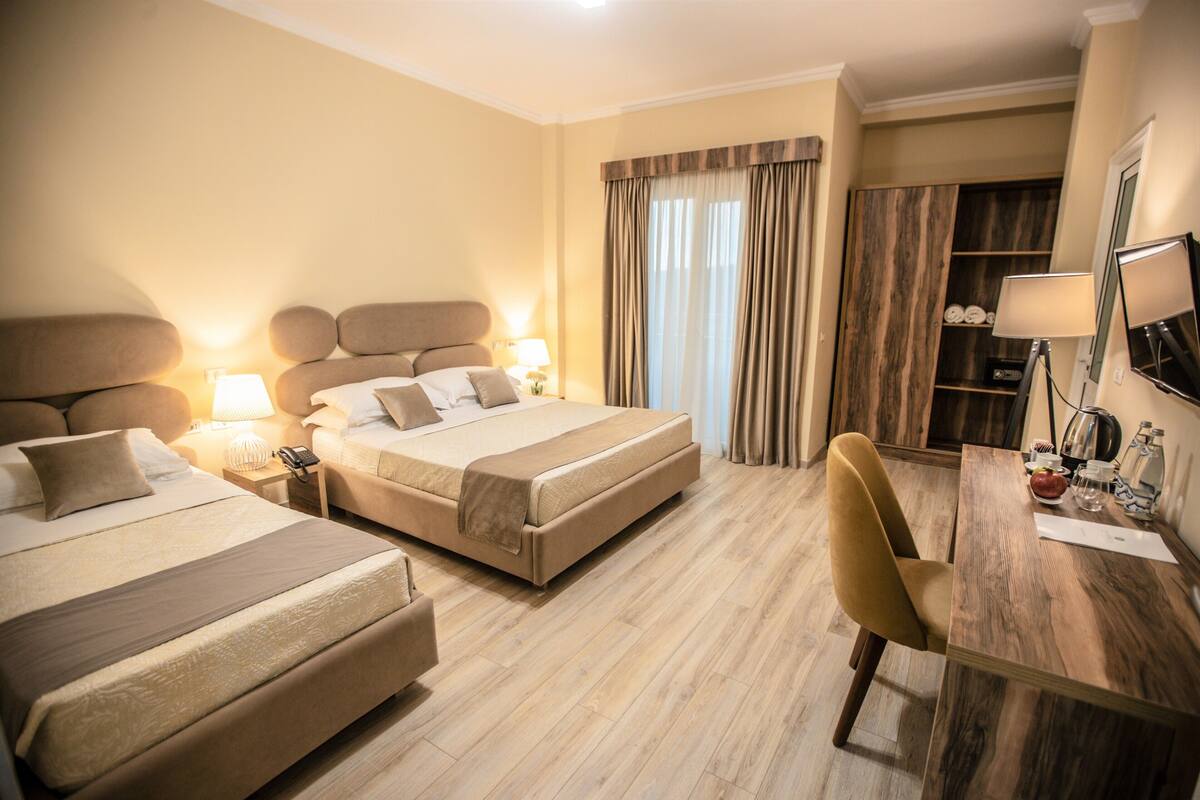 A hotel room with two beds, a desk, a chair, a wardrobe, and a mirror.
