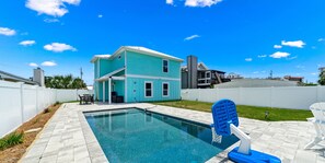 A swimming pool with a blue chair and a basketball hoop in a backyard with a house.